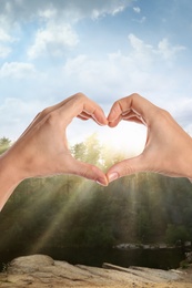 Woman making heart with hands outdoors on sunny day, closeup