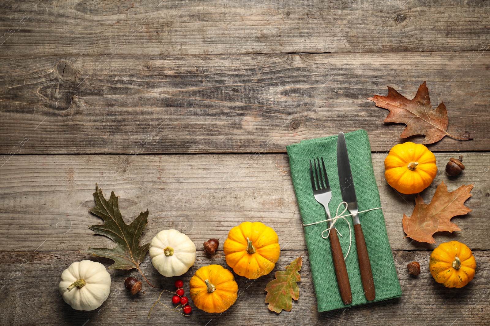 Photo of Cutlery, napkin and autumn decoration on wooden background, flat lay with space for text. Table setting