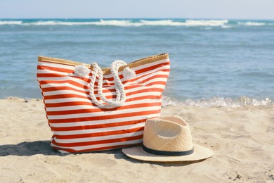Photo of Stylish striped bag with straw hat on sandy beach near sea