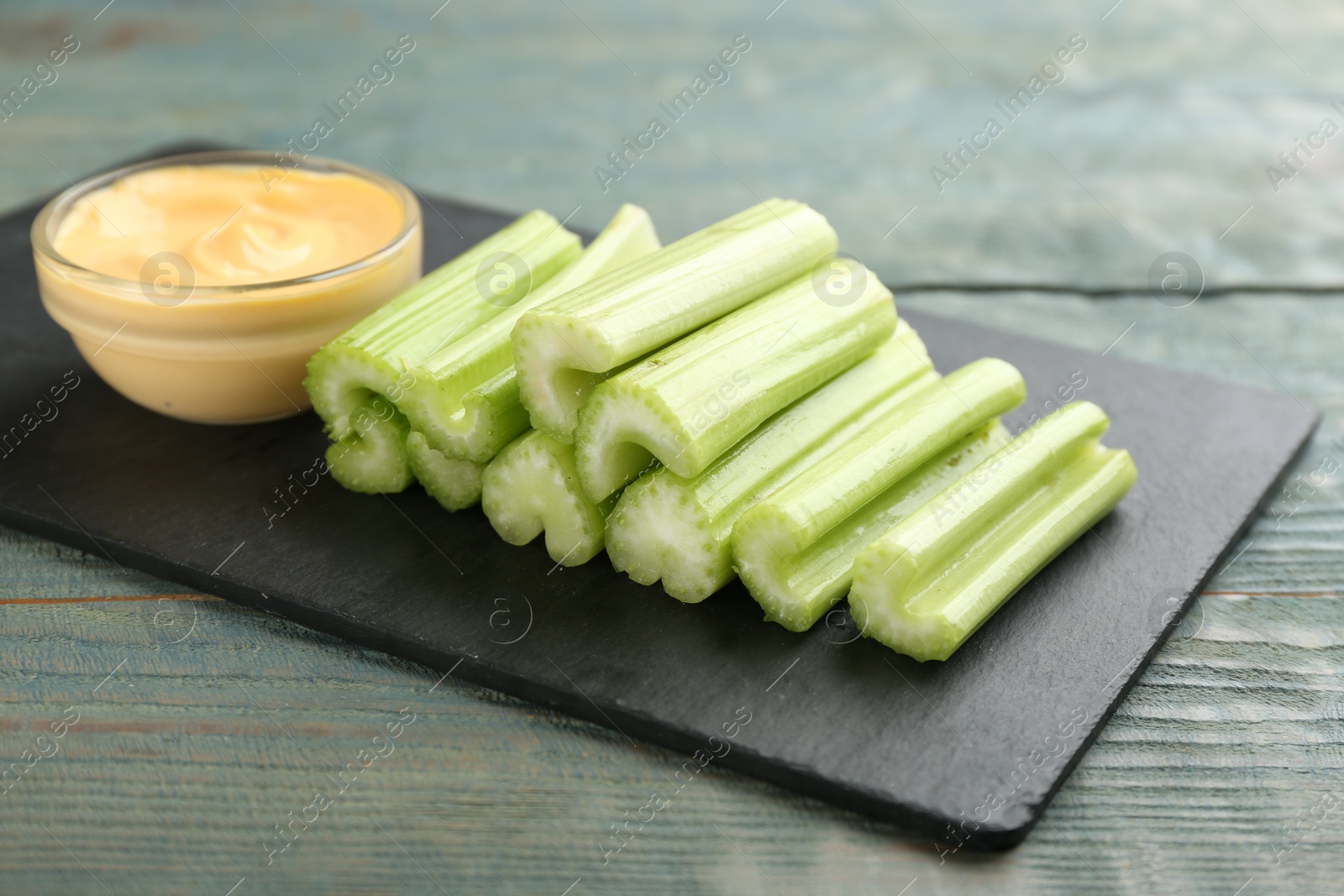 Photo of Celery sticks with dip sauce on light blue wooden table