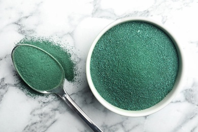 Photo of Bowl and spoon of spirulina algae powder on marble background, top view