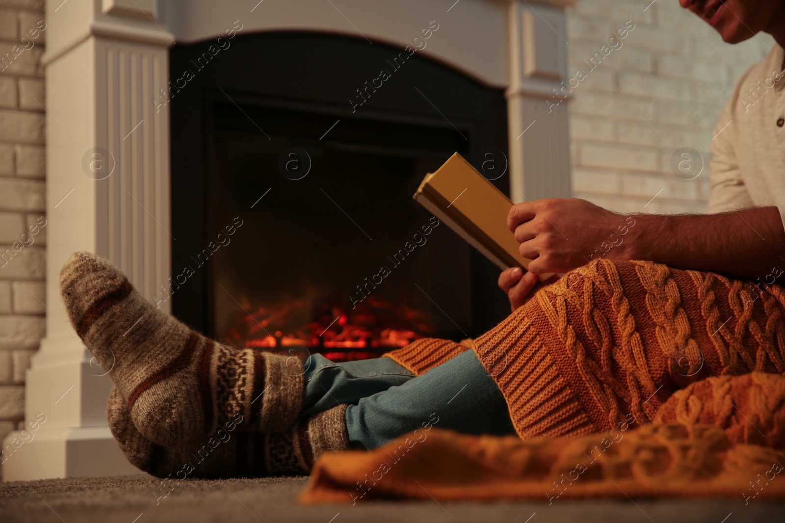 Photo of Man warming up with orange plaid while reading book at fireplace, closeup