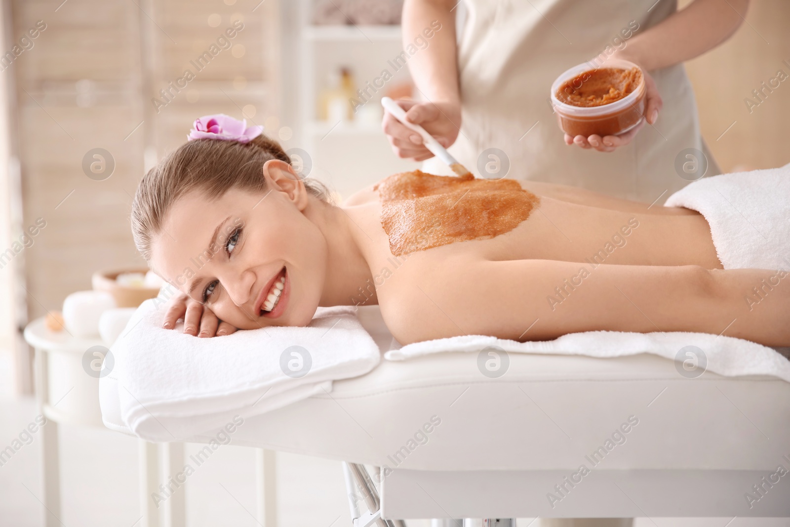 Photo of Beautiful young woman having massage with body scrub in spa salon