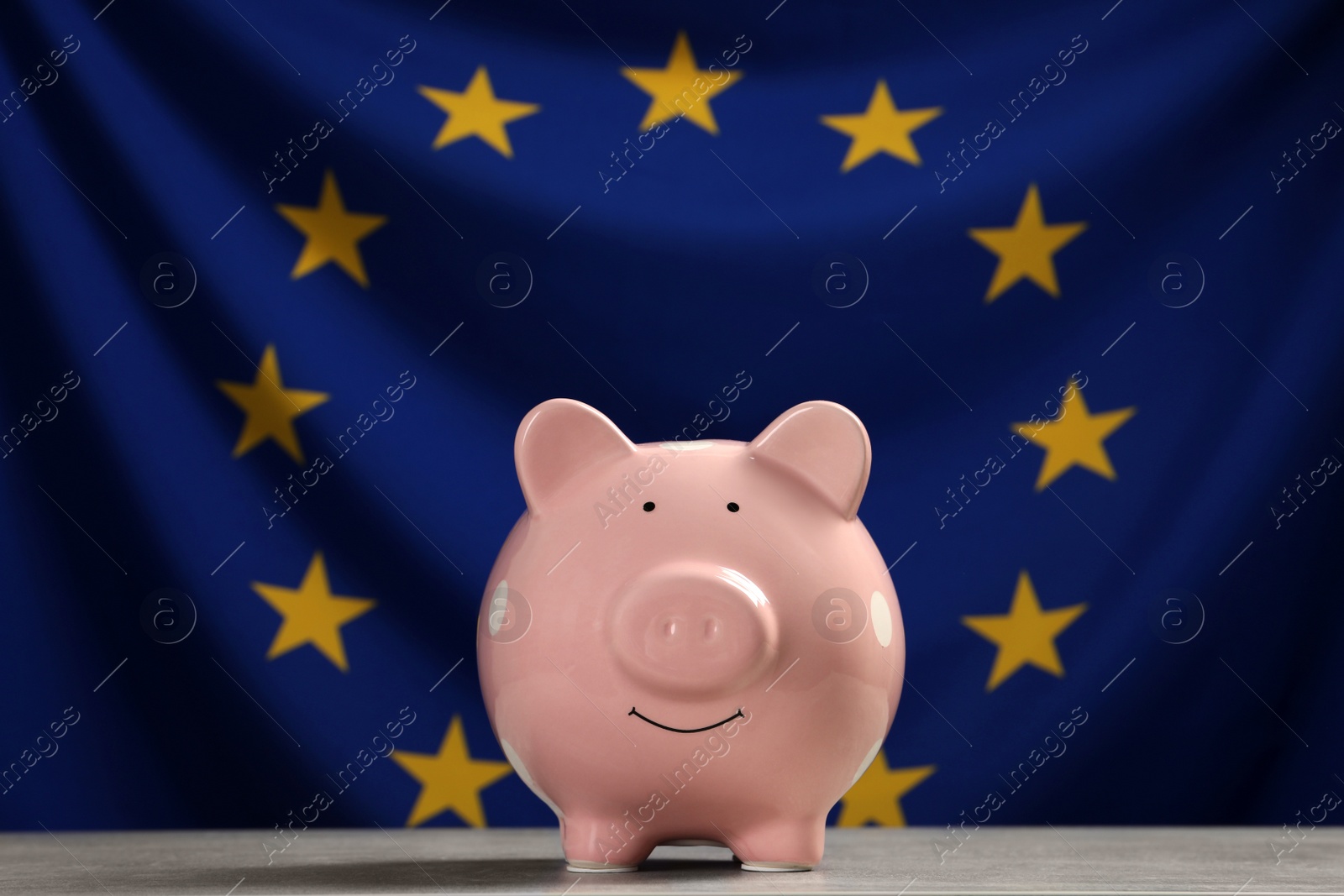 Photo of Pink piggy bank on light grey table against flag of European Union