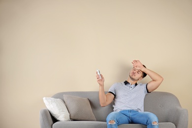 Young man with air conditioner remote suffering from heat at home