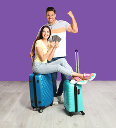 Happy couple with suitcases and tickets in passports for summer trip near purple wall. Vacation travel