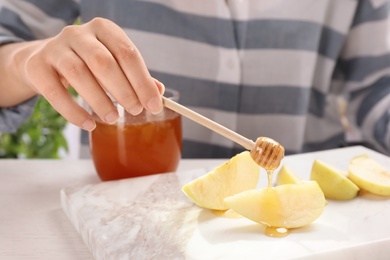 Photo of Woman pouring honey onto sliced apple at table