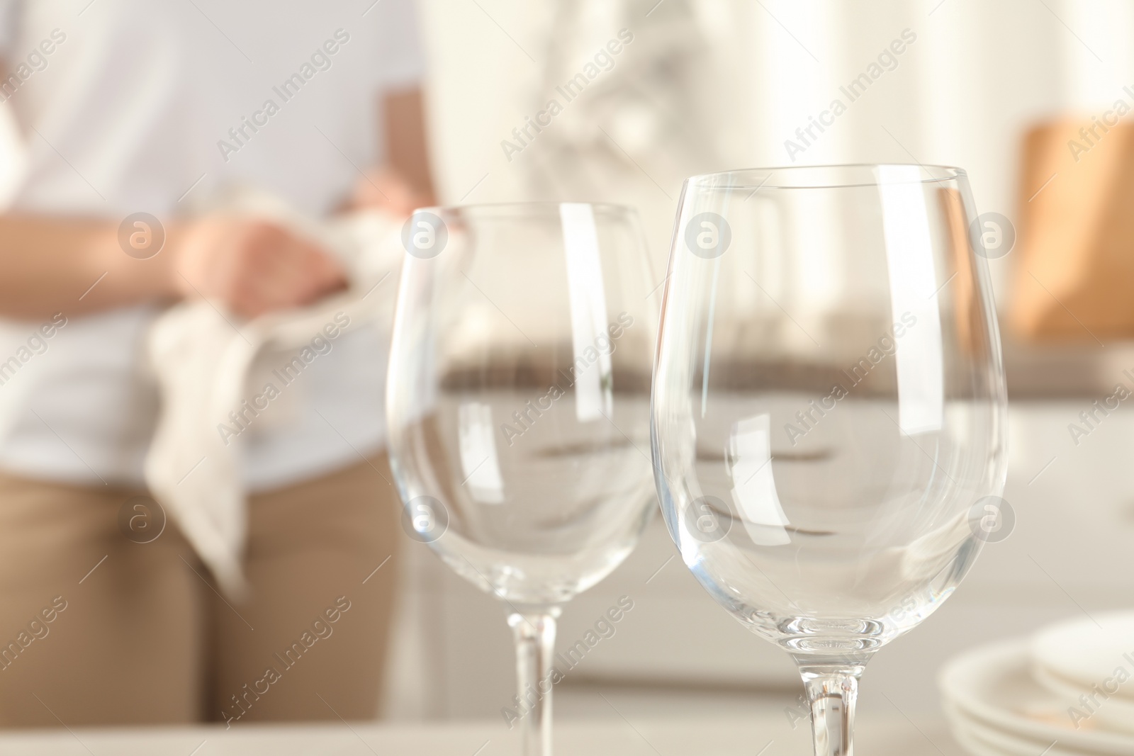 Photo of Woman wiping plate with towel in kitchen, focus on clean glasses