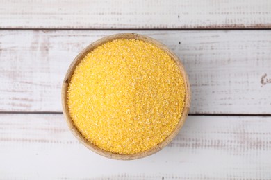 Photo of Raw cornmeal in bowl on light wooden table, top view