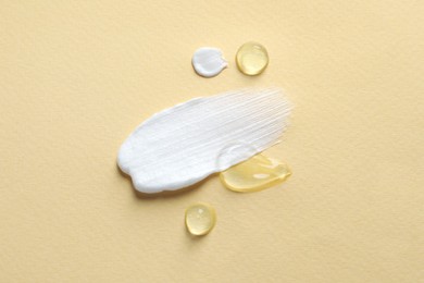 Samples of transparent gel and white cream on yellow background, flat lay