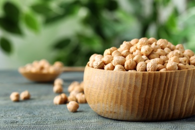 Photo of Raw chickpeas in bowl on blue wooden table, closeup. Space for text