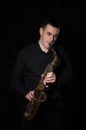 Young man playing saxophone on dark background