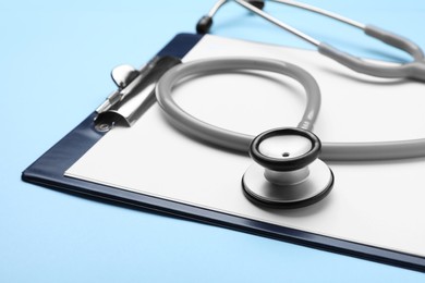 Photo of Stethoscope and clipboard on light blue background, closeup