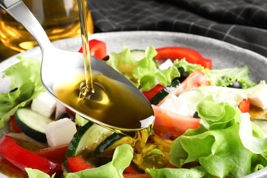 Photo of Adding cooking oil to delicious salad on table, closeup