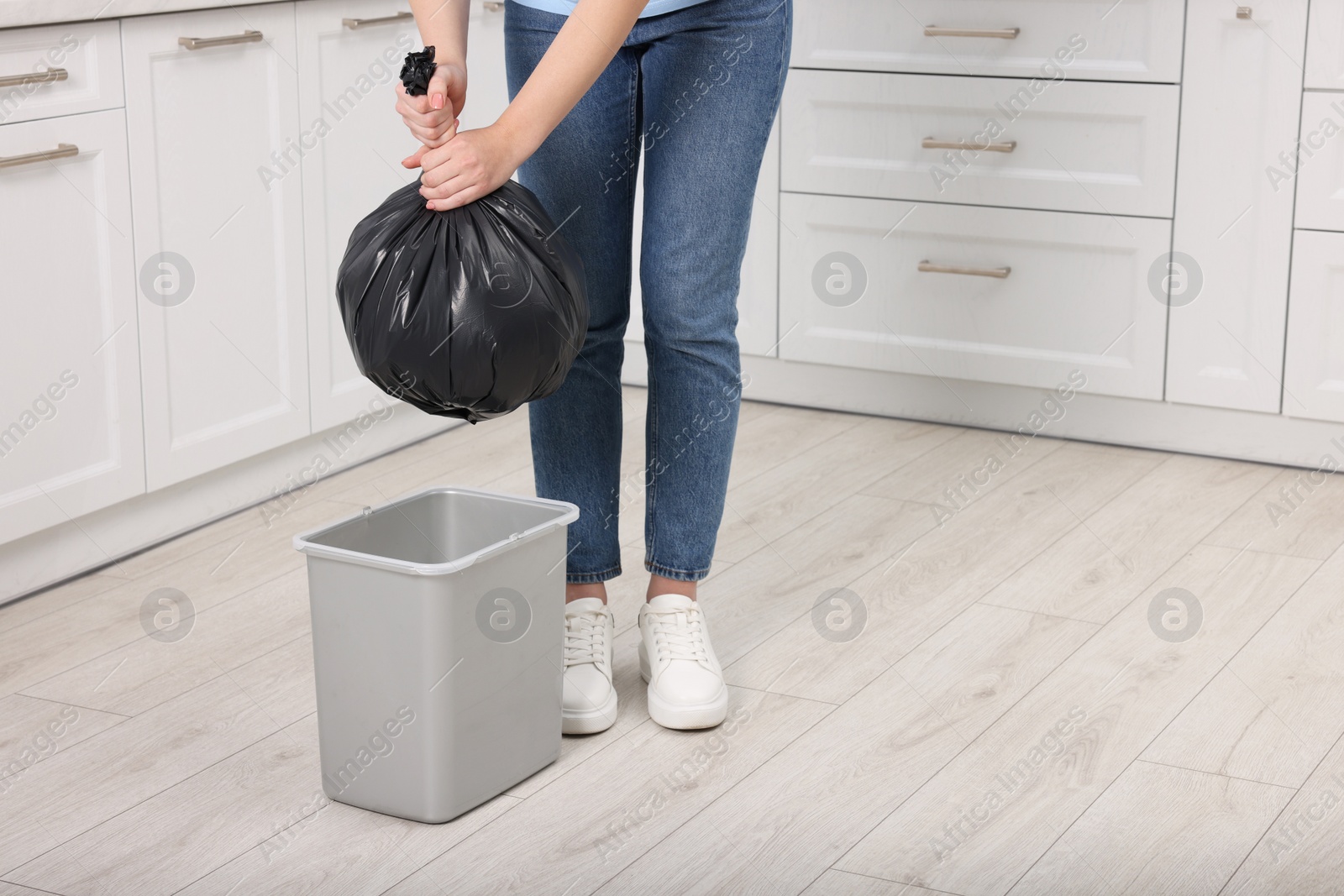 Photo of Woman taking garbage bag out of trash bin in kitchen, closeup. Space for text