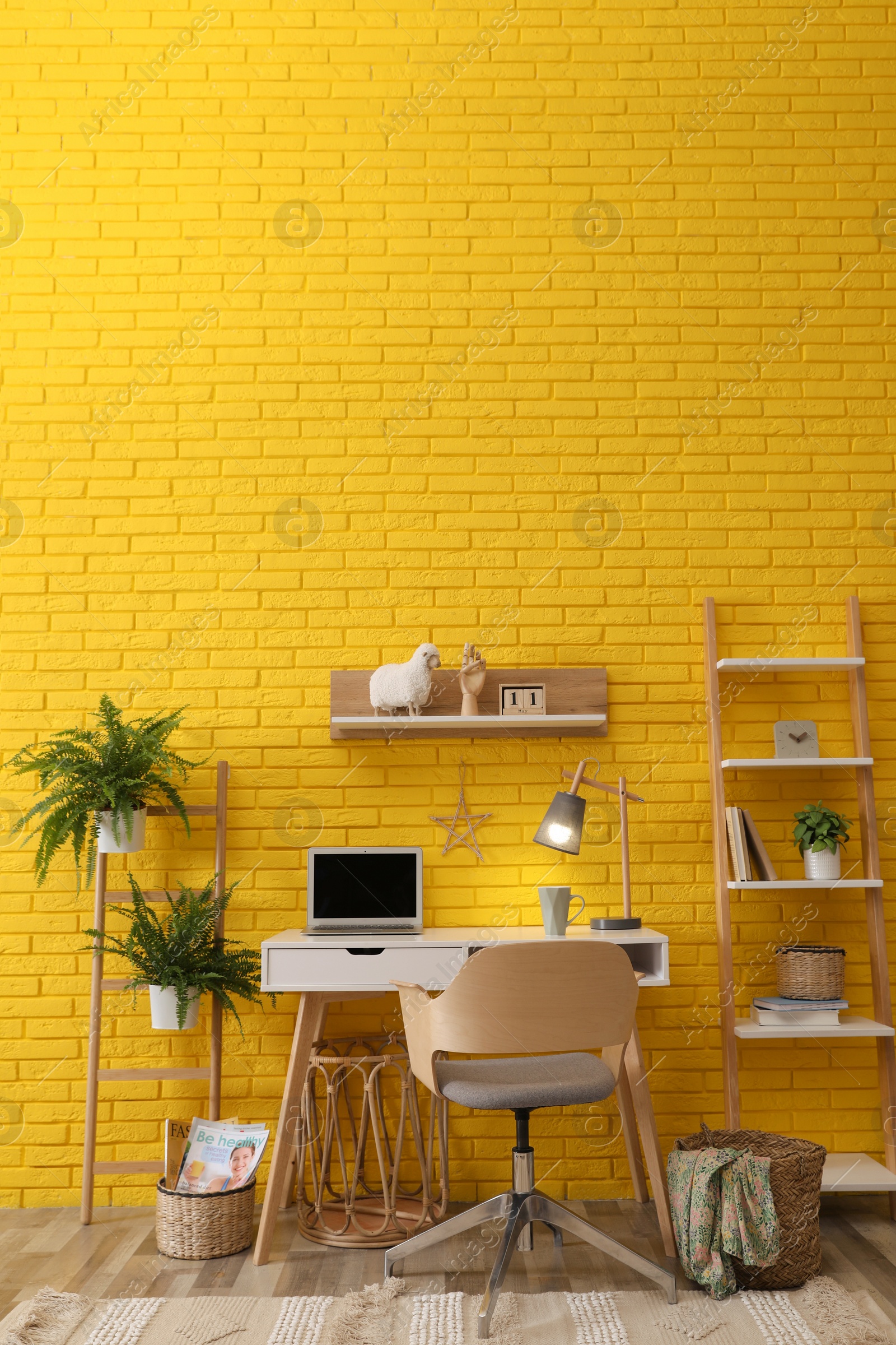 Photo of Modern workplace interior with wooden furniture and laptop near yellow brick wall