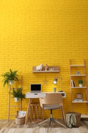 Modern workplace interior with wooden furniture and laptop near yellow brick wall