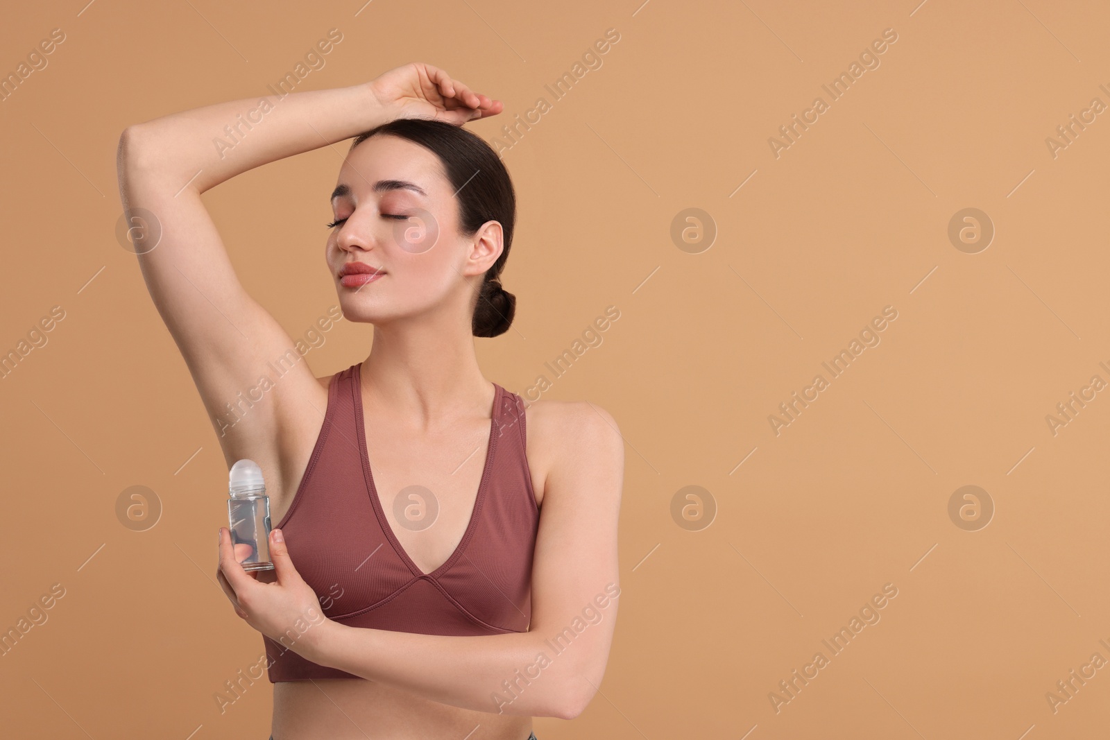 Photo of Beautiful woman applying deodorant on beige background, space for text