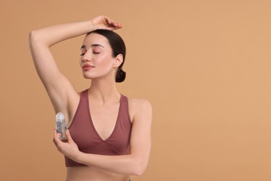 Beautiful woman applying deodorant on beige background, space for text