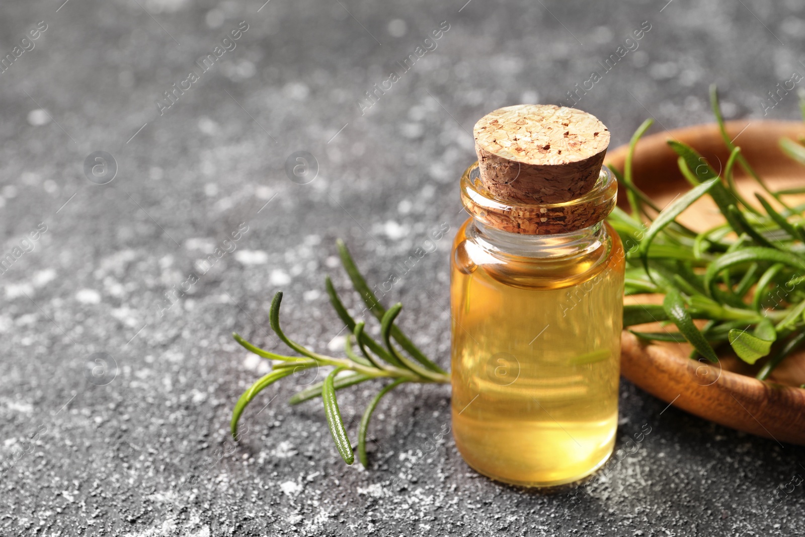 Photo of Bottle with essential oil and fresh rosemary on grey textured table, closeup. Space for text
