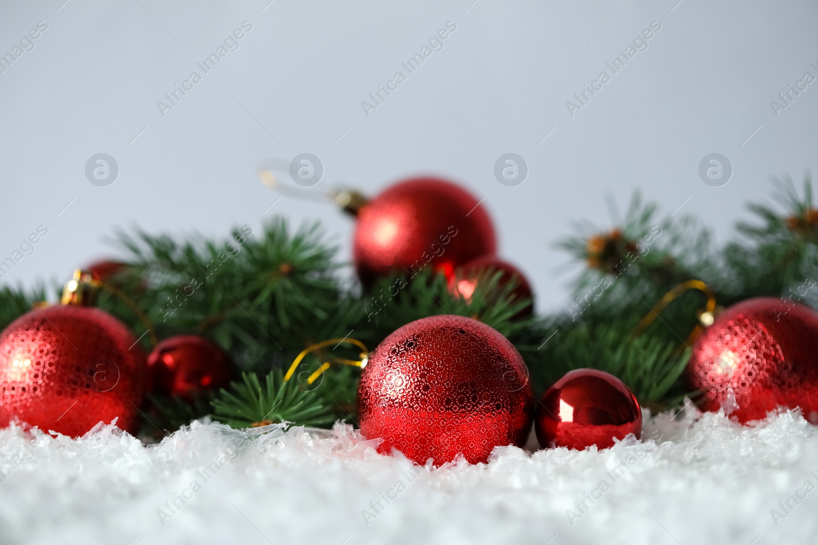 Photo of Beautiful Christmas balls and fir branches on snow against grey background. Space for text