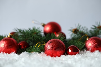 Photo of Beautiful Christmas balls and fir branches on snow against grey background. Space for text