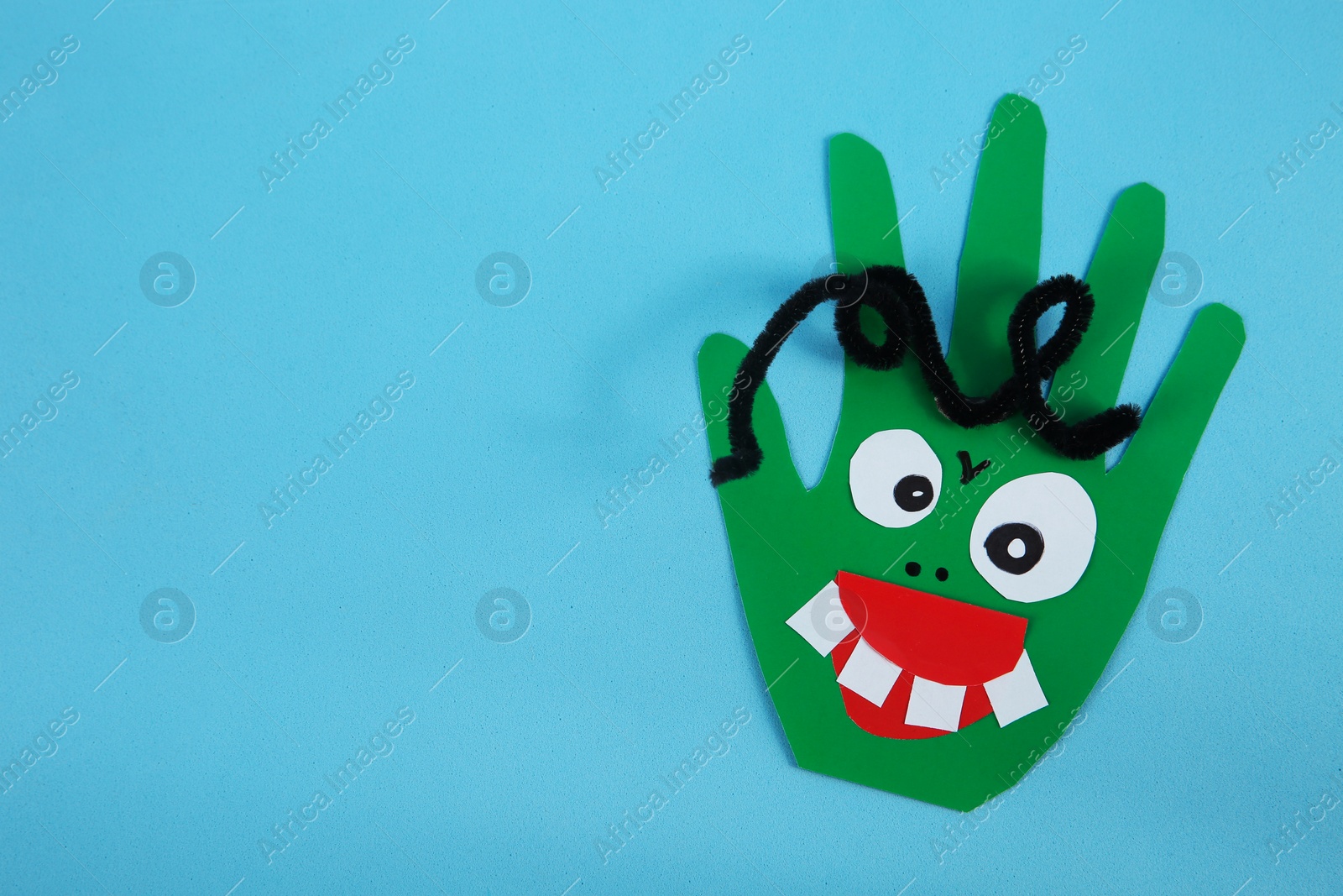 Photo of Funny green hand shaped monster on light blue background, top view with space for text. Halloween decoration