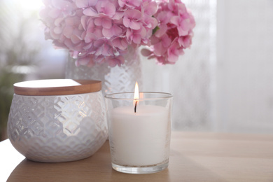 Burning candle and beautiful flowers on wooden table indoors