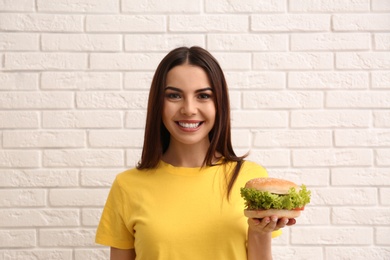 Photo of Young woman with tasty burger near brick wall