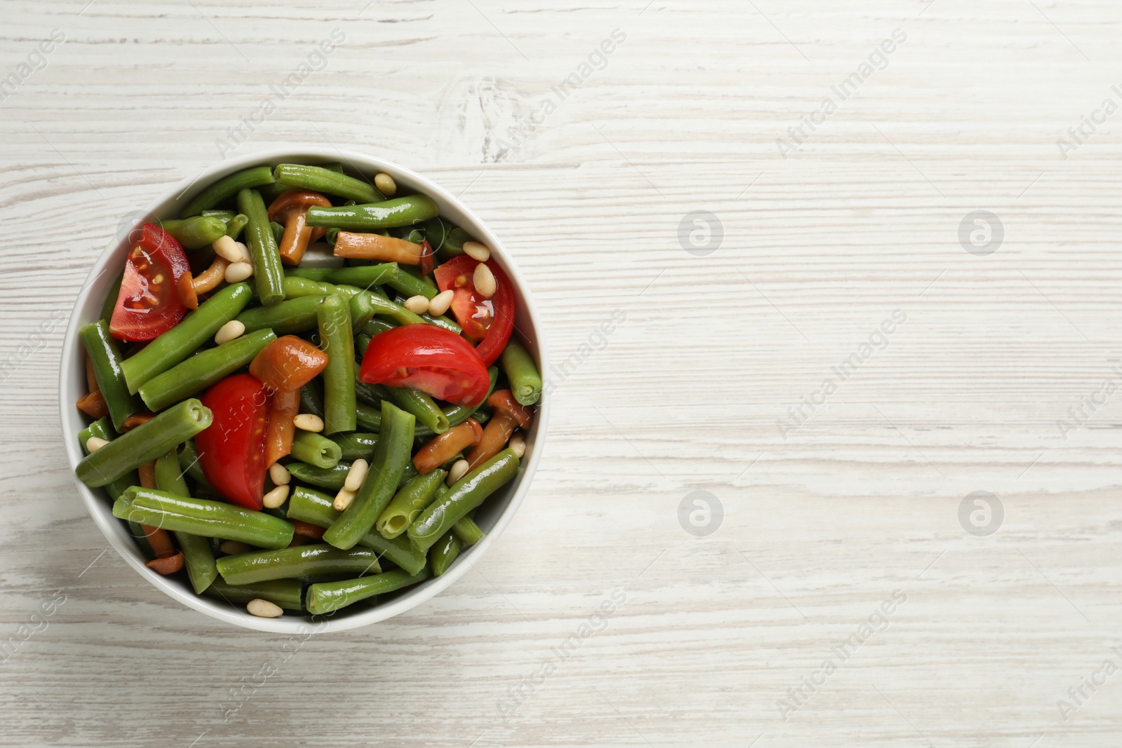 Photo of Delicious salad with green beans, mushrooms, pine nuts and tomatoes on white wooden table, top view. Space for text