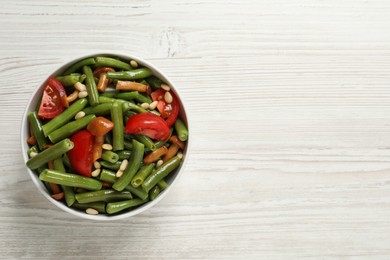 Delicious salad with green beans, mushrooms, pine nuts and tomatoes on white wooden table, top view. Space for text