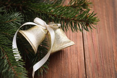 Photo of Bells with bow and fir branches on wooden table, closeup with space for text. Christmas decor