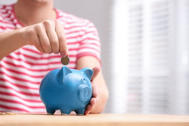 Man putting coin into piggy bank at wooden table, closeup. Space for text