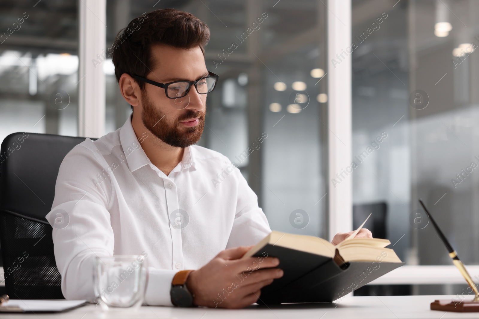 Photo of Handsome man reading book at table in office, space for text. Lawyer, businessman, accountant or manager