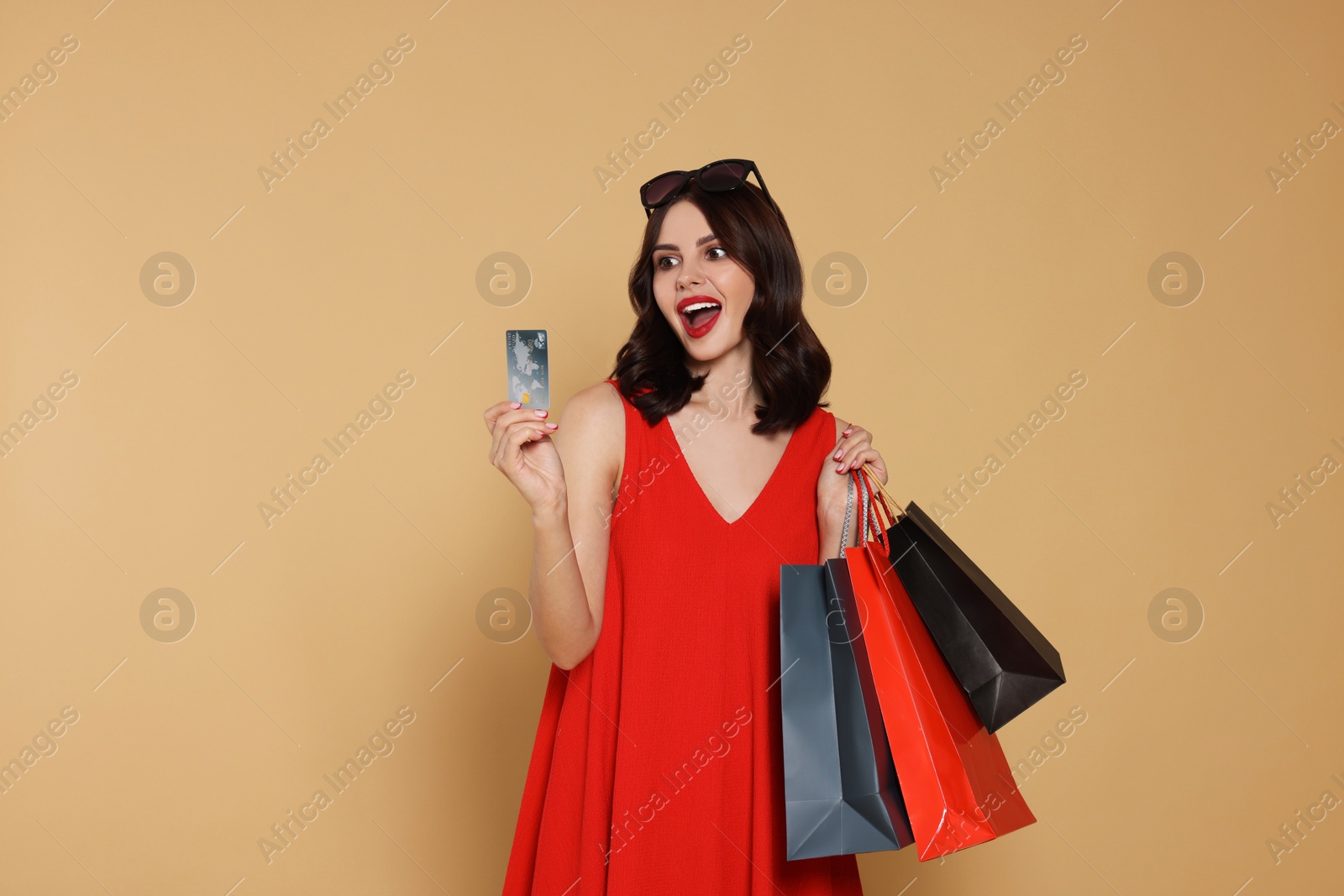 Photo of Emotional young woman with paper shopping bags and credit card on beige background