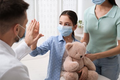 Mother with daughter visiting pediatrician in hospital. Wearing protective masks