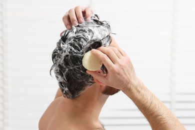Photo of Man washing his hair with solid shampoo bar in shower, closeup