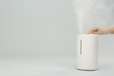 Photo of Woman using modern air humidifier on light grey background, closeup. Space for text