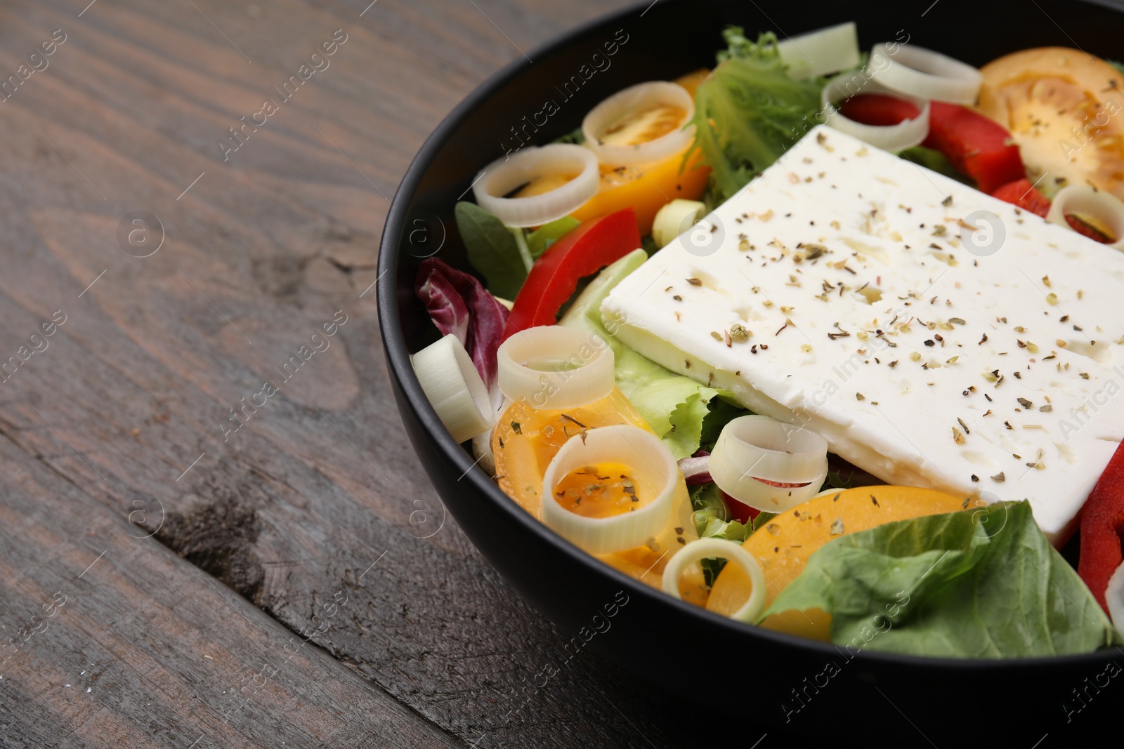 Photo of Bowl of tasty salad with leek and cheese on wooden table, closeup. Space for text