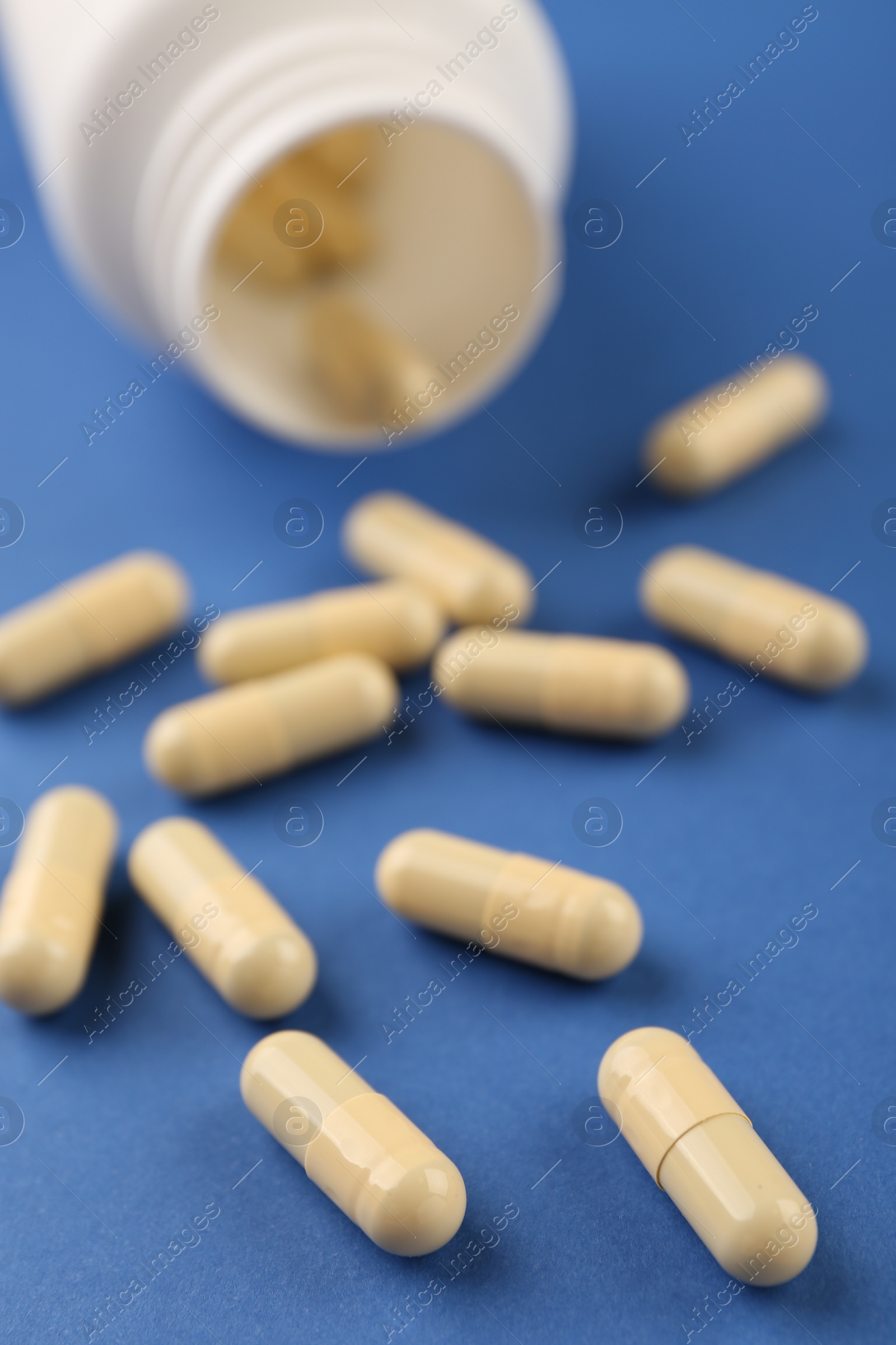 Photo of Bottle and vitamin capsules on blue background, closeup