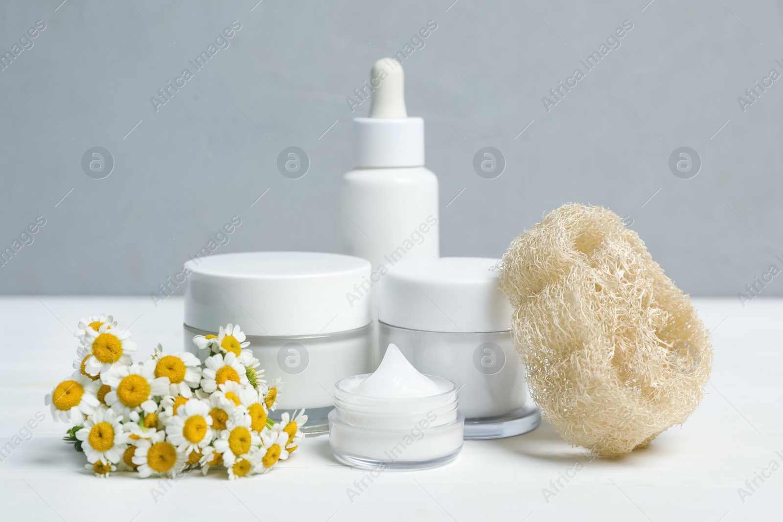 Photo of Set of cosmetic products, chamomiles and loofah on white table against grey background