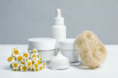 Set of cosmetic products, chamomiles and loofah on white table against grey background