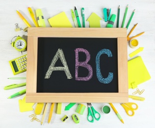 Photo of Small chalkboard with letters ABC and different school stationery on white wooden background, top view