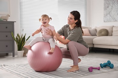 Photo of Mother doing exercise with her daughter on fitball at home