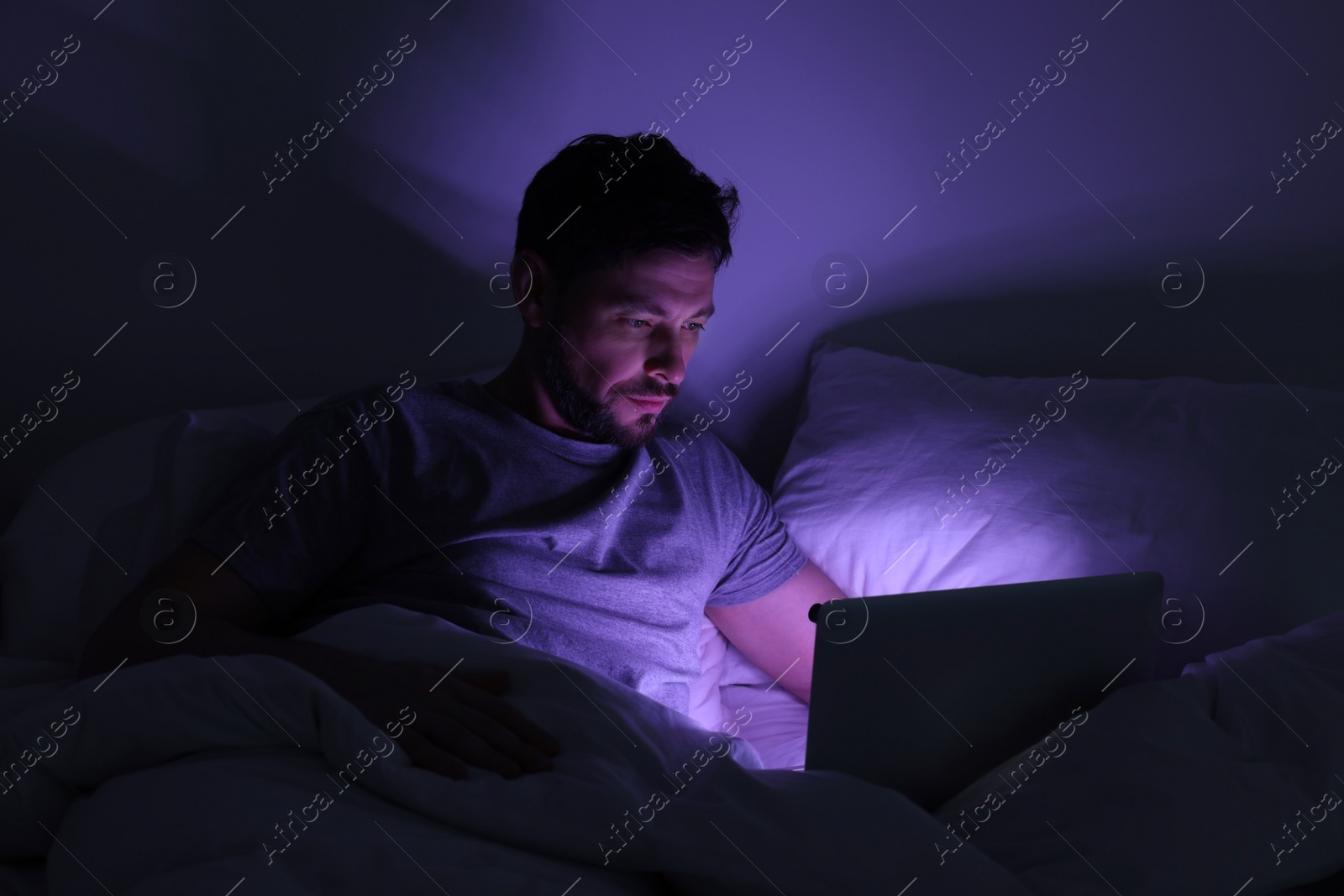 Photo of Man using laptop in bed at night. Internet addiction