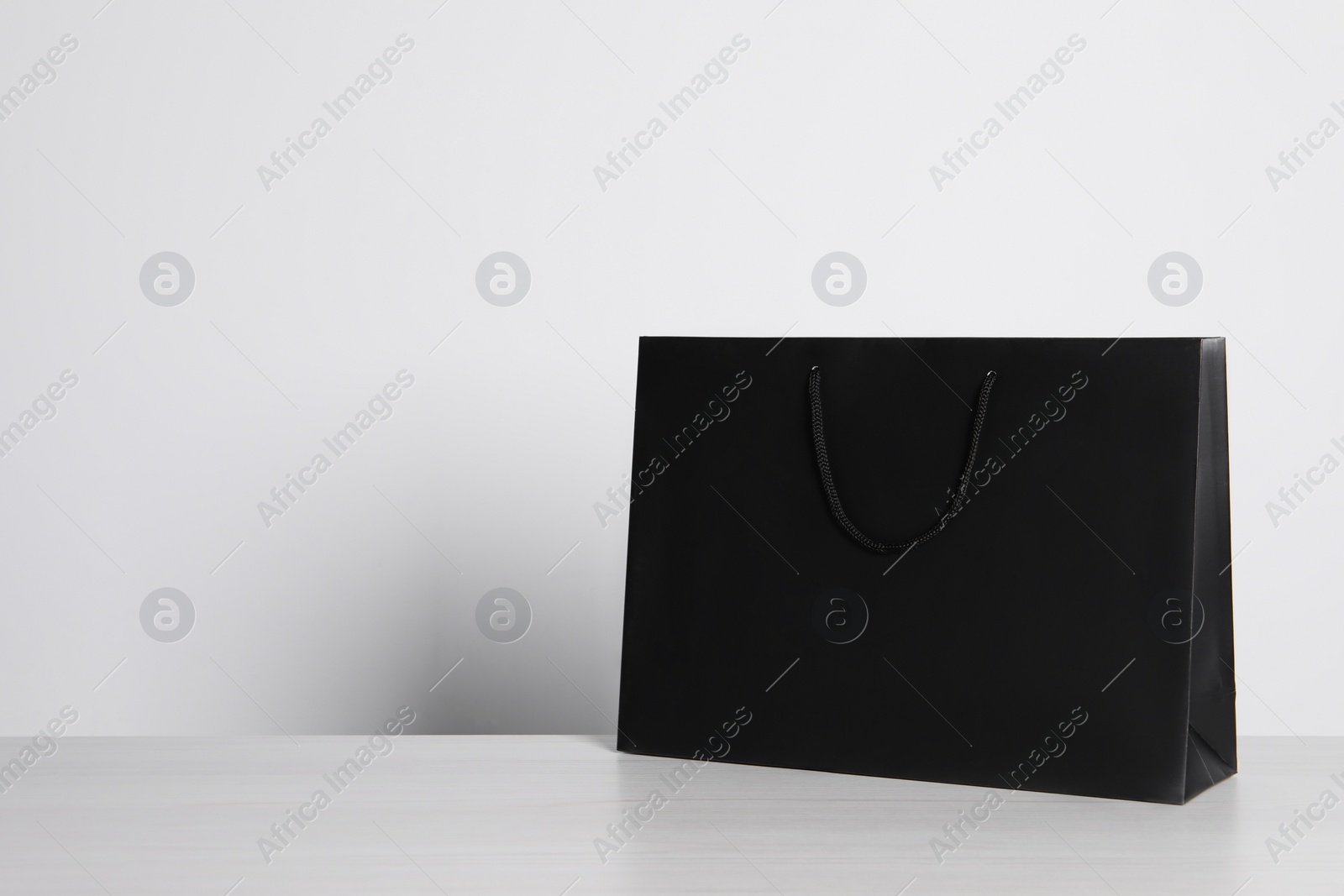 Photo of Black paper bag on white wooden table, space for text