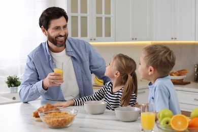 Photo of Father and his little children having breakfast at table in kitchen