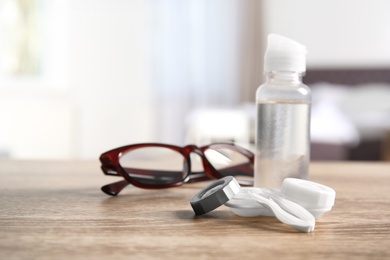 Photo of Contact lens case, tweezers, bottle of solution and glasses on table