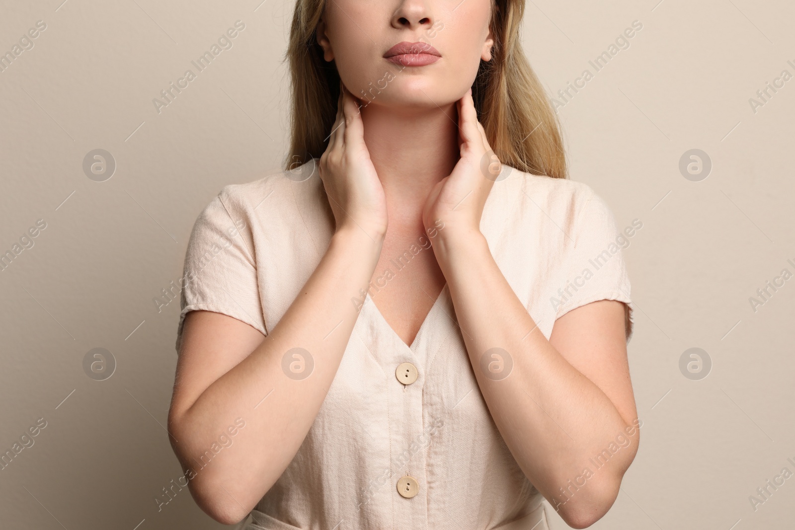 Photo of Young woman doing thyroid self examination on beige background, closeup