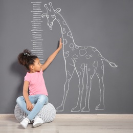 Photo of African-American child near grey wall with chalk giraffe drawing and height meter